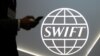 CANADA -- A man using a mobile phone passes the logo of global secure financial messaging services cooperative SWIFT at the SIBOS banking and financial conference in Toronto, Ontario, October 19, 2017