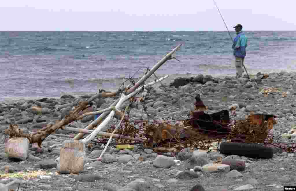A man fishes near rusted debris that has washed onto a beach on the shoreline of the French Indian Ocean island of La Reunion. On August 2, a small piece of metal debris found washed up on a beach on Reunion was taken into police custody. A flaperon, which help pilots control an aircraft in flight, will be analyzed to determine if the debris came from Malaysia Airlines Flight MH370, which disappeared without a trace 16 months ago with 239 passengers and crew on board. (Reuters/Jacky Naegelen)