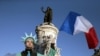 A man, dressed as the Statue of Liberty, holds up the French national flag at the Place de la Republique.