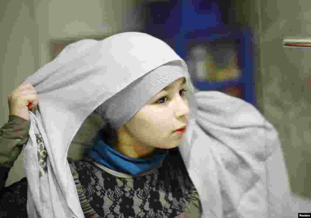 Sanaa (10) stavlja hidžab dok se priprema da krene u Islamsku nedjeljnu školu u Leytonu, istočni London. Ona povremeno nosi hidžab i tokom školskih dana. Njena majka Dalila kaže: &quot;Možda će već sljedeće godine Sanaa odlučiti da nosi hidžab svaki dan. Ona će sama odlučiti kada je taj trenutak da zauvijek pokrije glavu.&quot;