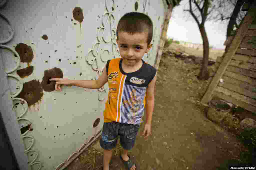Siyavus has two boys. One stands at the bullet-riddled door on his property.