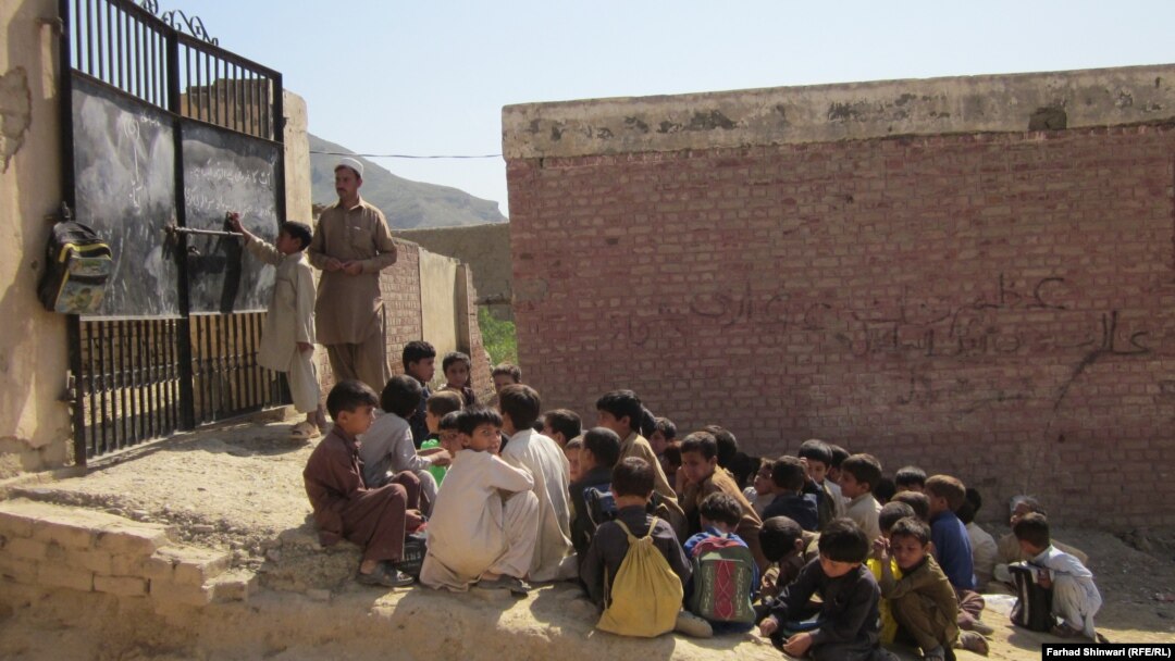 په خیبر کې د یو ړنګ ښوونځي زده کوونکي تر شنه اسمان لاندې زده کړې کوي او ښوونکی دروازه د لیکلو لپاره کاروي - پخوانی انځور. 