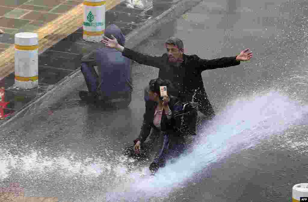 A Turkish woman shows her identity card next to another protestor as riot police use water cannon during clashes after hundreds of people tried to reach Ankara's main Kizilay Square to celebrate May Day in Ankara. (AFP/Adem Altan)