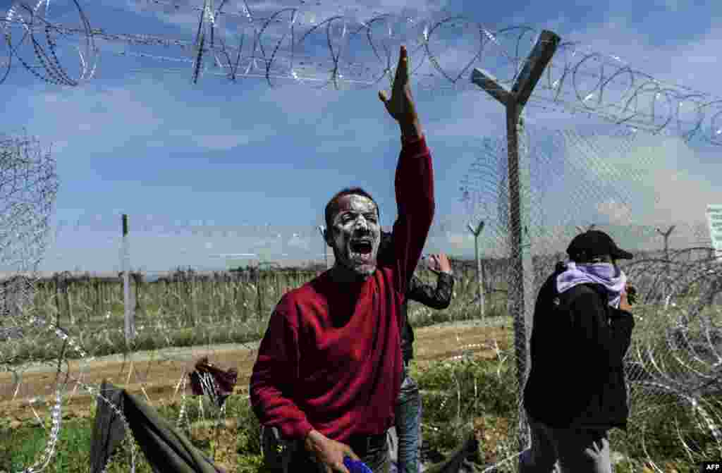 A man calls to other refugees and migrants to use a gap in wire fencing to cross the Greek border into Macedonia following clashes with Macedonian security forces. (AFP/Bulent Kilic)