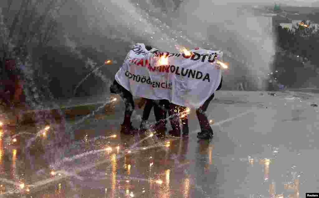 Demonstrators take cover from a police water cannon as fireworks, thrown by other protesters, explode around them during a demonstration against the opening of a new road in Ankara. (Reiters/Umit Bektas)