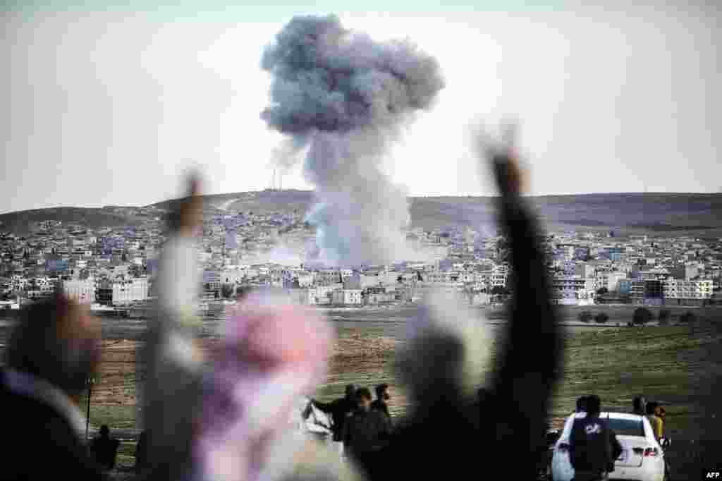 People in the southeastern Turkish village of Mursitpinar gesture as air strikes hit Kobani, across the border with Syria, on October 22. Kurdish pershmerga fighters were battling Islamic State militants for control of the town. (Bulent Kilic, AFP)