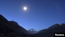 The first light of dawn illuminates Mount Everest as the moon shines above and a toilet block is seen in the foreground in the Tibet Autonomous Region, China