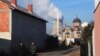 Men walk along the street in front of an Orthodox Church and a mosque as smoke billows out of the towers of a coal-fired power plant in Obilic, near Pristina, on December 5.