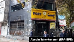 Iranians walk past next to a post office that was burned and destroyed during the protests over increasing fuel price by government in city of Shahriar, Alborz province, November 20, 2019