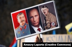 Транспарант с изображением Иосифа Сталина, Владимира Путина и Адольфа Гитлера во время акции протеста против вторжения России в Украину, 27 февраля 2022 г.