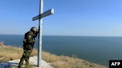 Украинский военнослужащий молится у креста, установленного на берегу моря близ города Мариуполя. Октябрь 2014 года. 