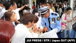 Сотрудник служб безопасности Японии инструктирует людей возле железнодорожной станции в Осаке после подземных толчков. 18 июня 2018 года.