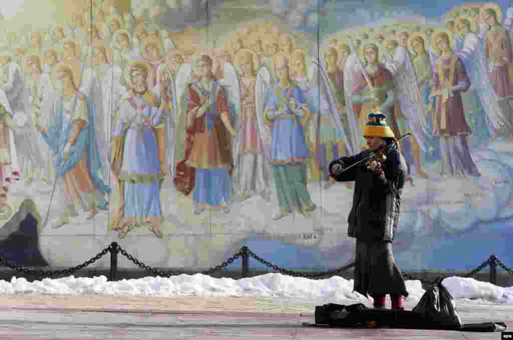 A young woman plays a violin to collect money in front of Mikhailovsky Cathedral frescoes in downtown Kyiv, Ukraine. (epa/Sergey Dolzenko)
