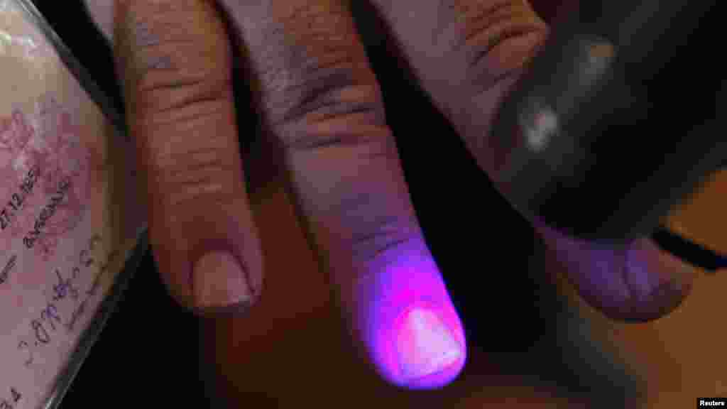 An election official checks a voter&#39;s fingers for invisible ink at a polling station in the village of Sartichala.