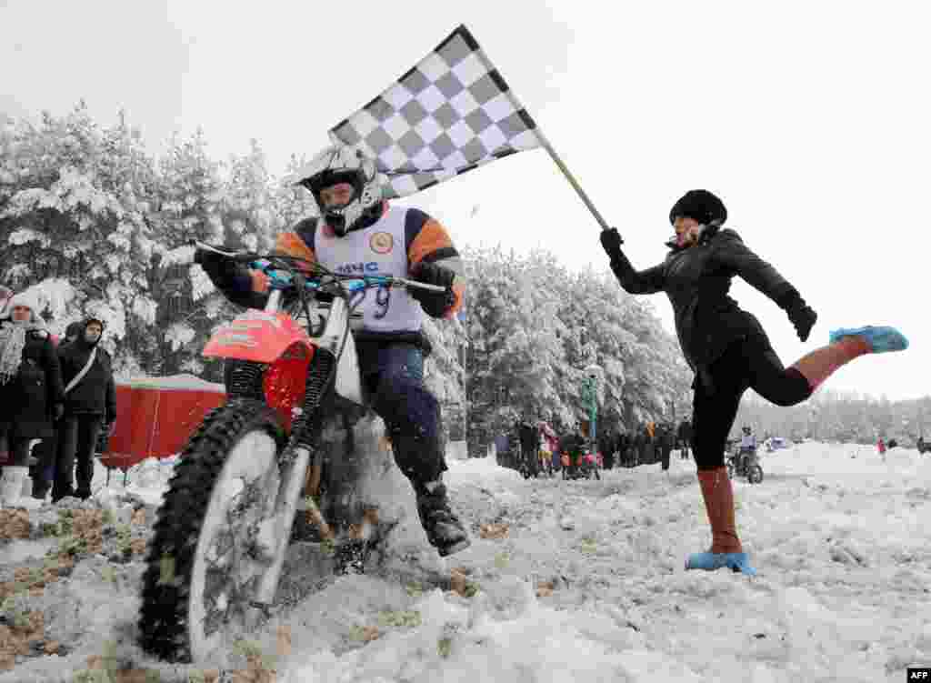 A motorcyclist passes a checkered-flag bearer during a snowbound race in the woods near Radoshkovichi, Belarus. (AFP/Viktor Drachev)