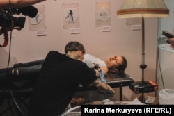 Илья Расписной набивает татуировку посетительнице выставки