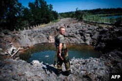Separatist înarmat lângă craterul unei bombe în Donețk.
