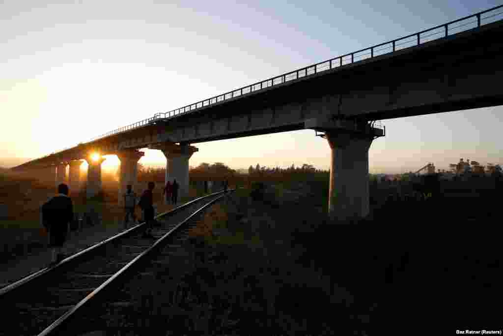 People walk along train tracks in front of a bridge, built for SGR railway trains near the town of Athi River, Kenya, February 13, 2019.