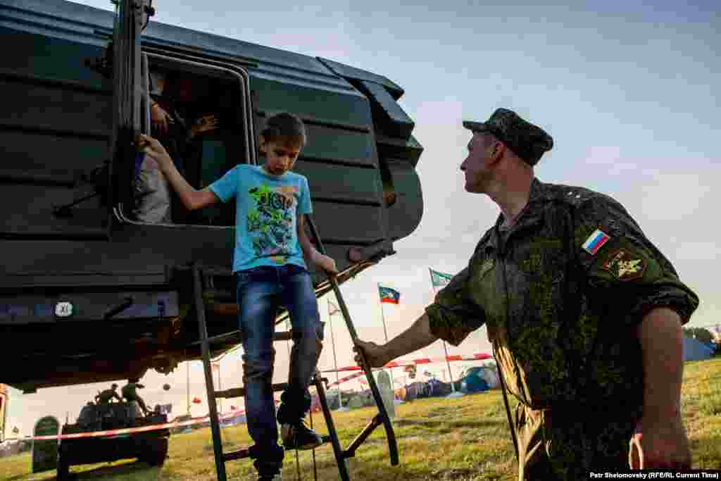 A serviceman helps a child step down after exploring the inside of a military vehicle.