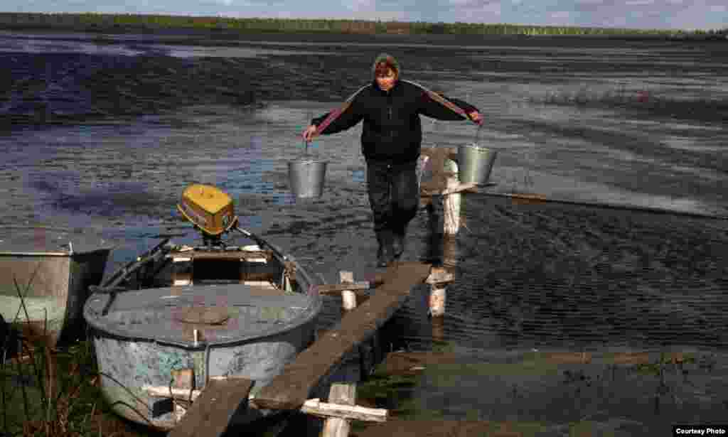 Тюменская область, Россия.&nbsp; Женщина несет на плечах коромысло с ведрами с водой из реки
