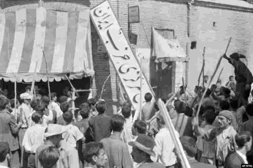 A crowd of demonstrators tears down the sign of the Iran Party, part of Mossadegh's National Front, at its headquarters on August 19.