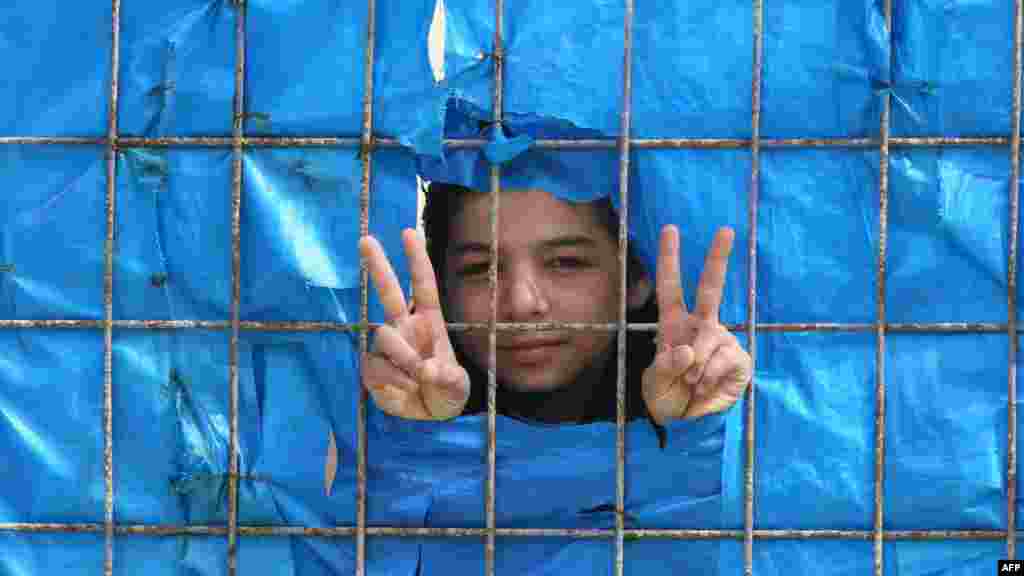A young Syrian refugee flashes the &quot;peace&quot; sign from behind a fence at a refugee camp in Yayladagi, Turkey.