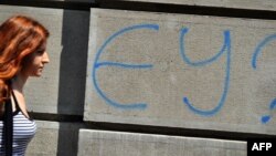 A woman walks past graffiti reading "EU?" in downtown Belgrade. (file photo)