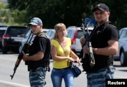 O femeie trece pe lângă doi separatiști înarmați în orășelul Șahtiorsk.