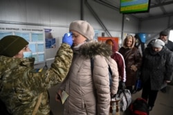 A Ukrainian border guard checks the temperature of a woman waiting to enter Ukraine from territory controlled by Russia-backed separatists in the Donetsk region.