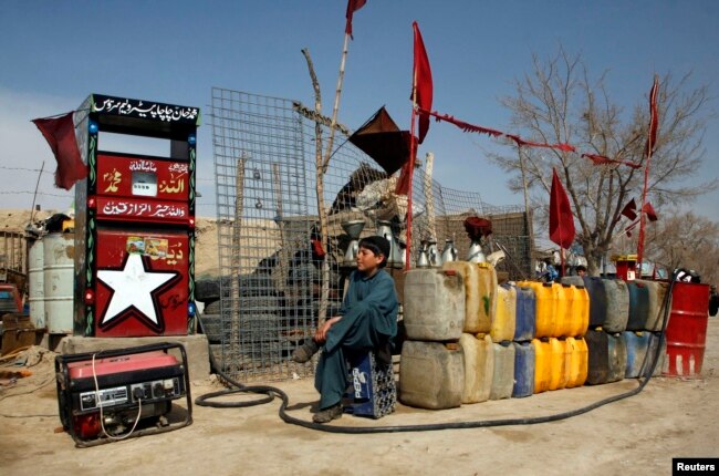 A boy sits next to plastic canisters filled with petrol that he says was brought from Iran, while waiting for customers at a roadside petrol station on the outskirts of Quetta.