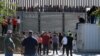 АКШ менен Мексиканын ортосундагы Сан-Исидро чек ара бекетинде күтүп турган адамдар. 25-ноябрь, 2018-жыл. 