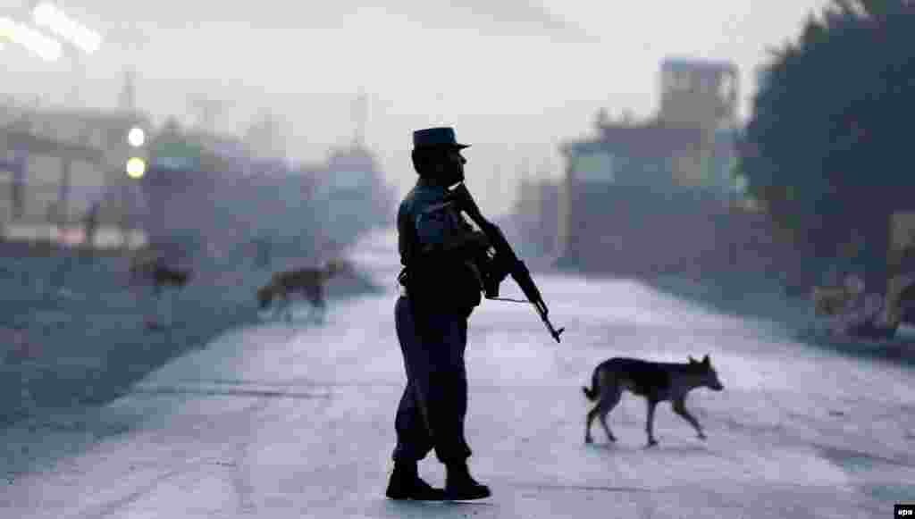 An Afghan police officer secures the road leading to a Kabul guesthouse frequented by foreigners that came under attack by the Taliban. Police said one attacker died when his vehicle detonated and two other militants were killed by police in a gunbattle. One police officer was also killed. (epa/Hedayatullah Amid)