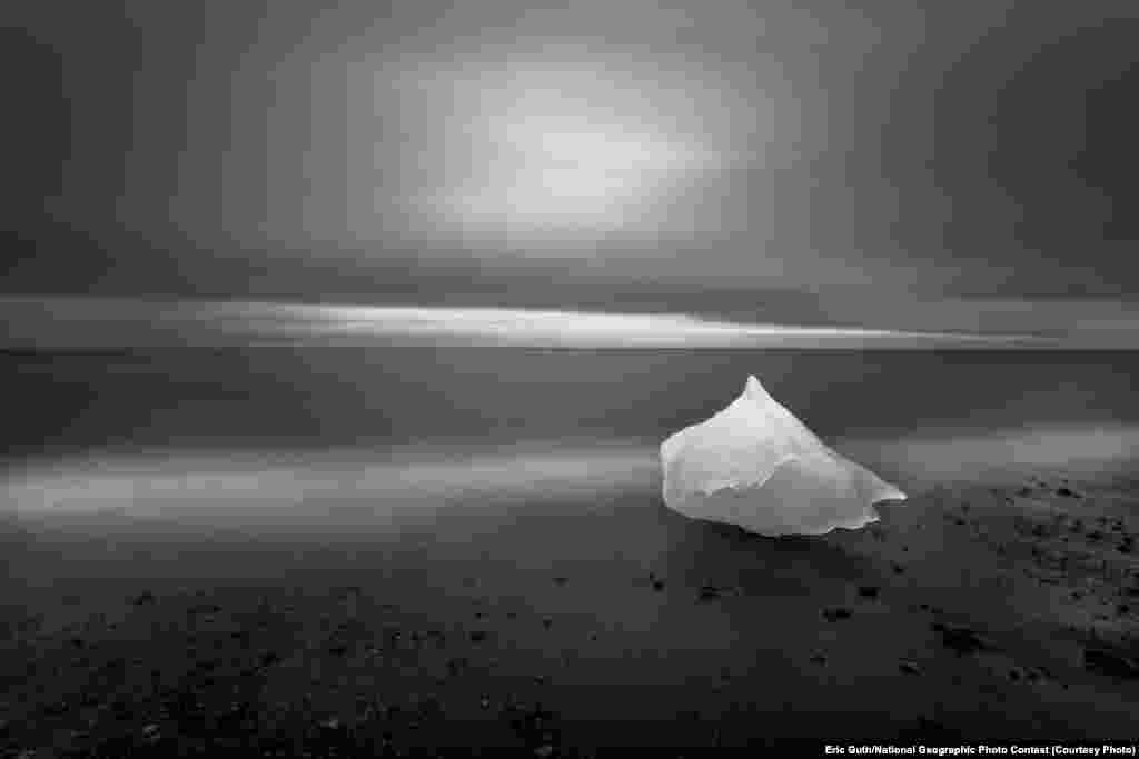 HONORABLE MENTION: East Of Iceland (Just east of Jokulsarlon Lagoon, Iceland) -- Glacial ice washes ashore after calving off the Breioeamerkurjoekull glacier on Iceland&#39;s eastern coast. During the waning light of summer, this image was created over the course of a four-minute exposure while the photographer backlit the grounded glacial ice with a headlamp for two of those four minutes. (Caption by photographer Eric Guth)