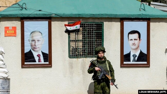 Руски военен стои на пост между портретите на сирийския президент Башар ал-Асад (вдясно) и руския президент Владимир Путин (вляво), висящи пред пост за охрана на контролно-пропускателния пункт Wafideen в покрайнините на Дамаск, 1 март 2018 г.