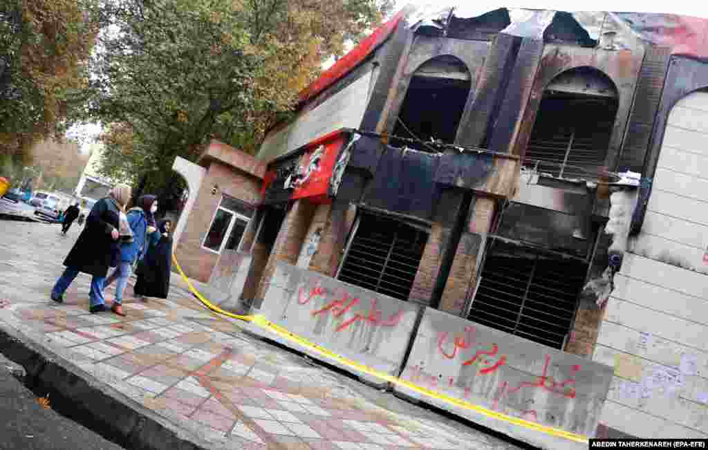 Women pass a branch of the Iranian Shahr Bank that was torched during protests in Shahriar.