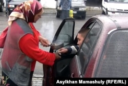 Женщина просит милостыню на автостоянке в Алматы.
