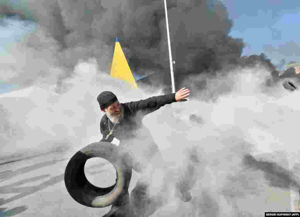 An Orthodox priest throws a tire as activists clash with volunteer servicemen trying to protect municipal workers.