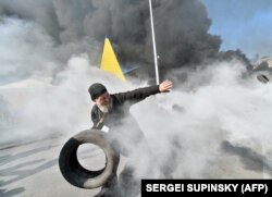 Un preot ortodox aruncă un cauciuc în timpul ciocnirilor din 7 august dintre manifestanții de pe Maidan și forțele de ordine.