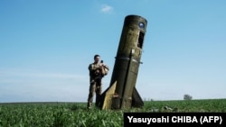 Украинский военный осматривает разгонную степень упавшей в поле на Харьковщине российской баллистической ракеты, 25 апреля 2022 года