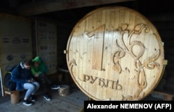 A couple sits next to a huge wooden Russian ruble coin in the center of the Siberian city of Tomsk on September 8.