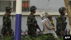 Китайские солдаты сопровождают женщину-мусульманку в городе Урумчи в провинции Синьцзян