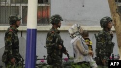 Китайские солдаты сопровождают женщину-мусульманку в городе Урумчи в провинции Синьцзян.