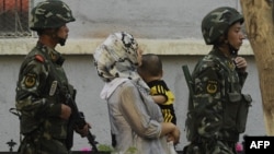 Вооруженные сотрудники китайских силовых структур ведут уйгурскую женщину с ребенком. Урумчи, июль 2010 года.
