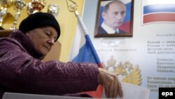 Женщина опускает бюллетень в урну на избирательном участке, где на стене висит портрет президента России Владимира Путина. Москва, 18 сентября 2016 года.