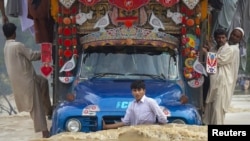 A boy hangs on to the front of a cargo truck while passing through a flooded road in Risalpur, in Pakistan's Nowshera district, on July 30.