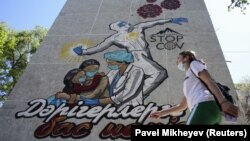 COVID-19 вирусына қарсы күресіп жатқан дәрігерлердің құрметіне сурет салынған көпқабатты тұрғын үйдің қасынан өтіп бара жатқан маска таққан адам. Алматы, 24 сәуір 2020 жыл.