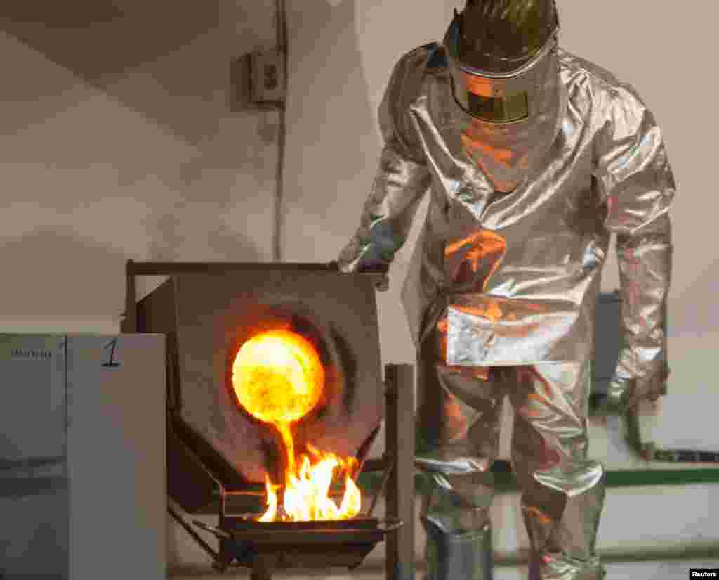 A worker wearing heatproof suit pours molten gold from a crucible into a mould in a workshop of Altyntau gold mine extraction factory.
