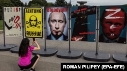 Жена снима постери, изобразяващи Владимир Путин, по време на изложба в Киев, 9 август 2022 г.