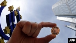 Еуропа орталық банкінің штаб-пәтері алдындағы еуро валютасының белгісі жанында түсірілген суреттегі адамның қолында 1 еуролық монета көрсетілген. Франкфурт, Германия, 29 сәуір, 2010 ж.