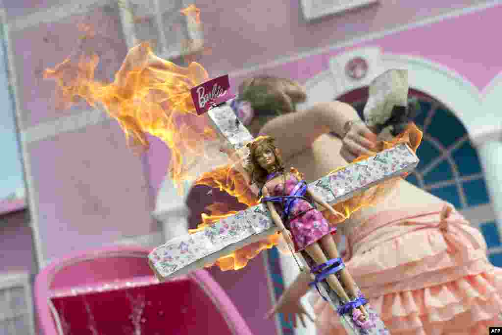 A Femen activist holds a burning crucifix with a Barbie doll affixed to it during a protest action in front of the so-called Barbie Dreamhouse in Berlin, the first life-sized mansion dedicated to the doll in Europe. Berlin feminists are mobilizing against the 2,500-square-meter mansion, which they call a sexist icon. (AFP/Barbara Sax)